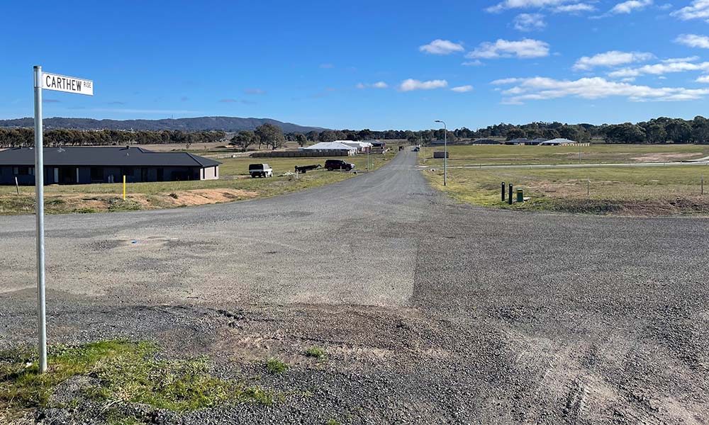 The Ararat East Development Zone. The foreground shows a gravel and asphalt intersection with a street sign pointing down the paved Carthew Rise which runs to the horizon. A number of houses and cars can be seem amongst grassland.