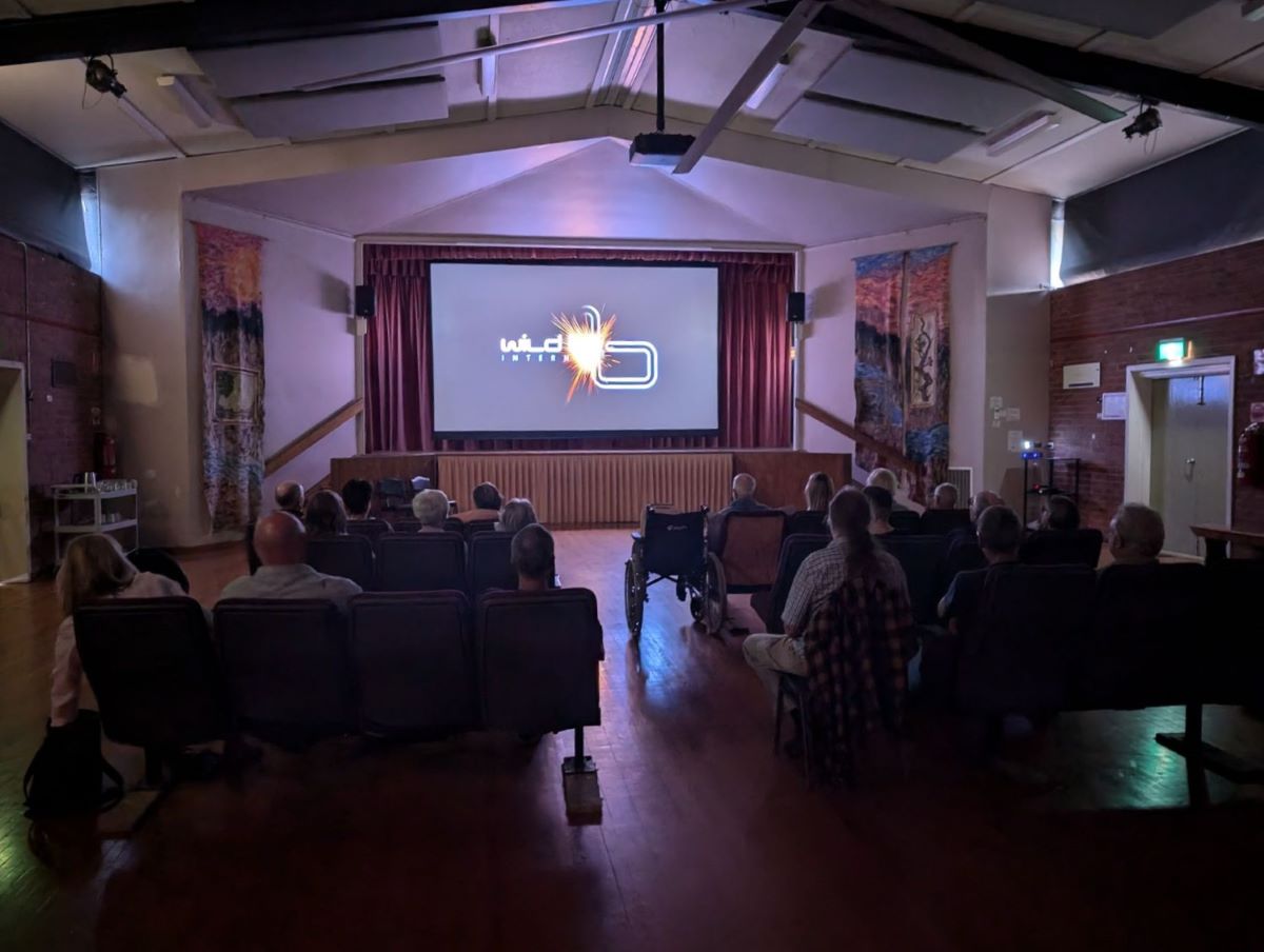 People sitting in a darkened hall watching a film on large screen. 