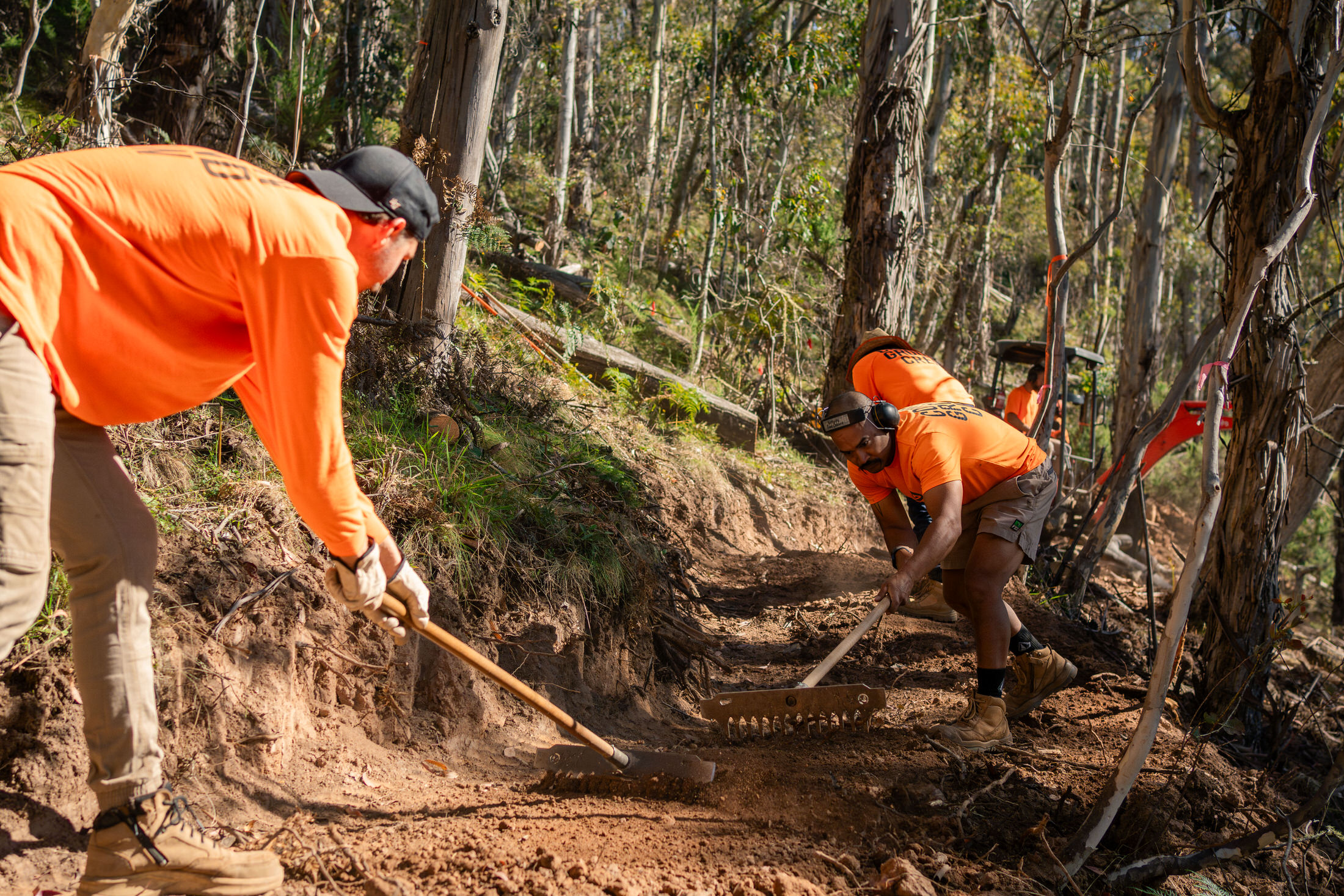 Two people in orange tops with handheld construction tools working on trail. Picture: Flow Mountain Bike