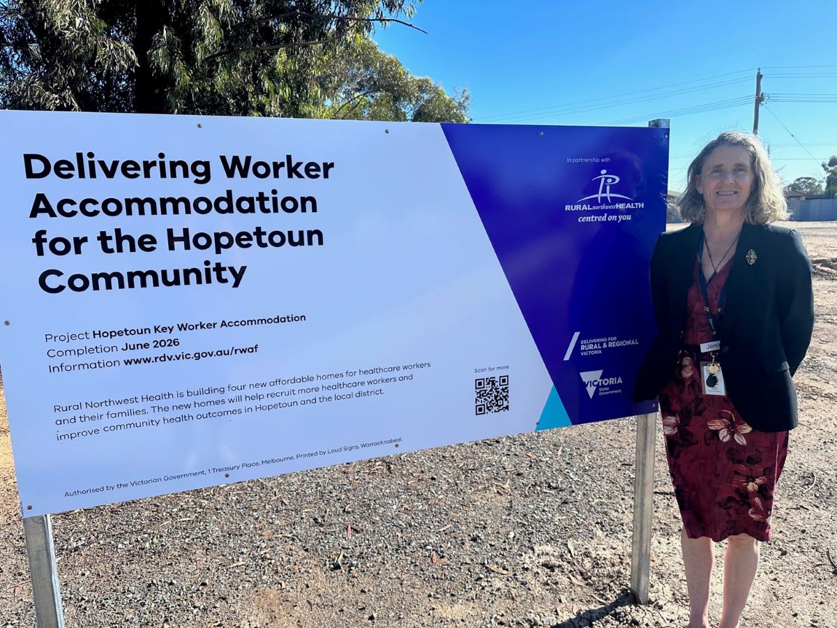 A woman standing beside a sign promoting the Regional Worker Accommodation Project.