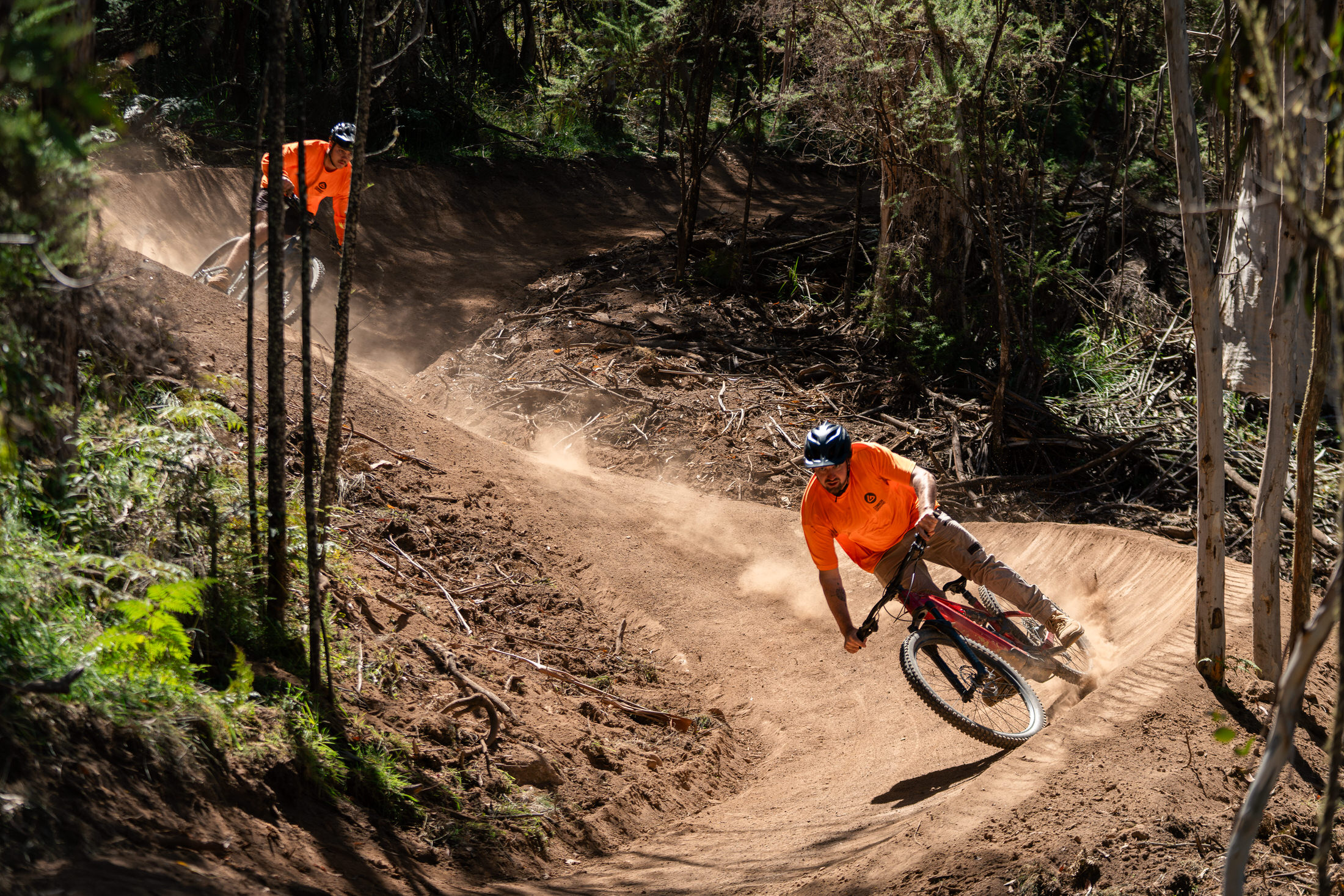 Two people in orange tops riding mountain bikes on a downhill trail. Picture: Flow Mountain Bike