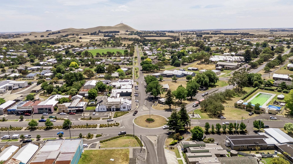 Aerial view of Mortlake, with the township in the foreground of the image and rolling hills with scattered collections of trees visible in the background.